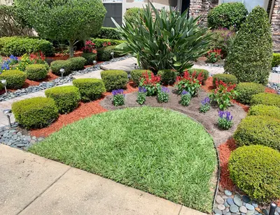 Landscaped front garden with trimmed shrubs, flowers, river rock and a lawn island