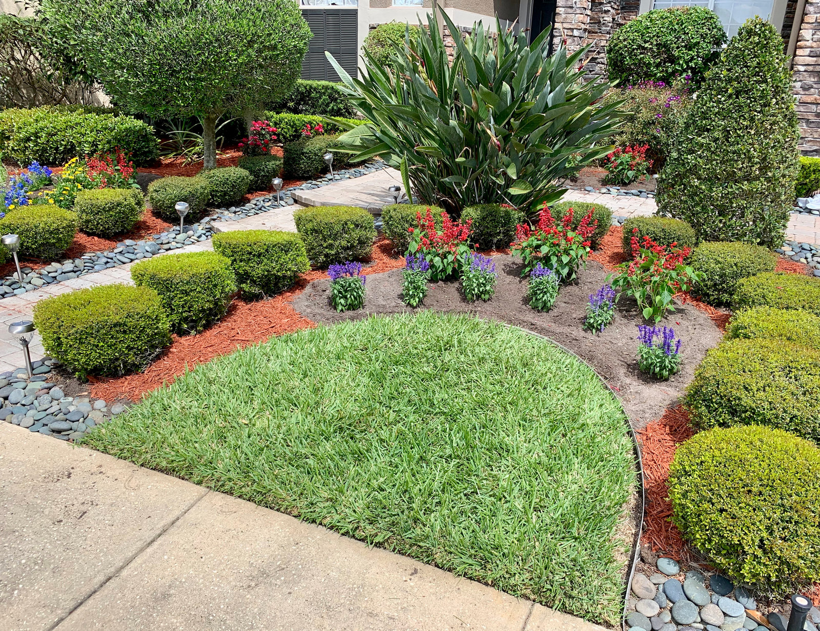 Landscaped front garden with trimmed shrubs, flowers, river rock and a lawn island
