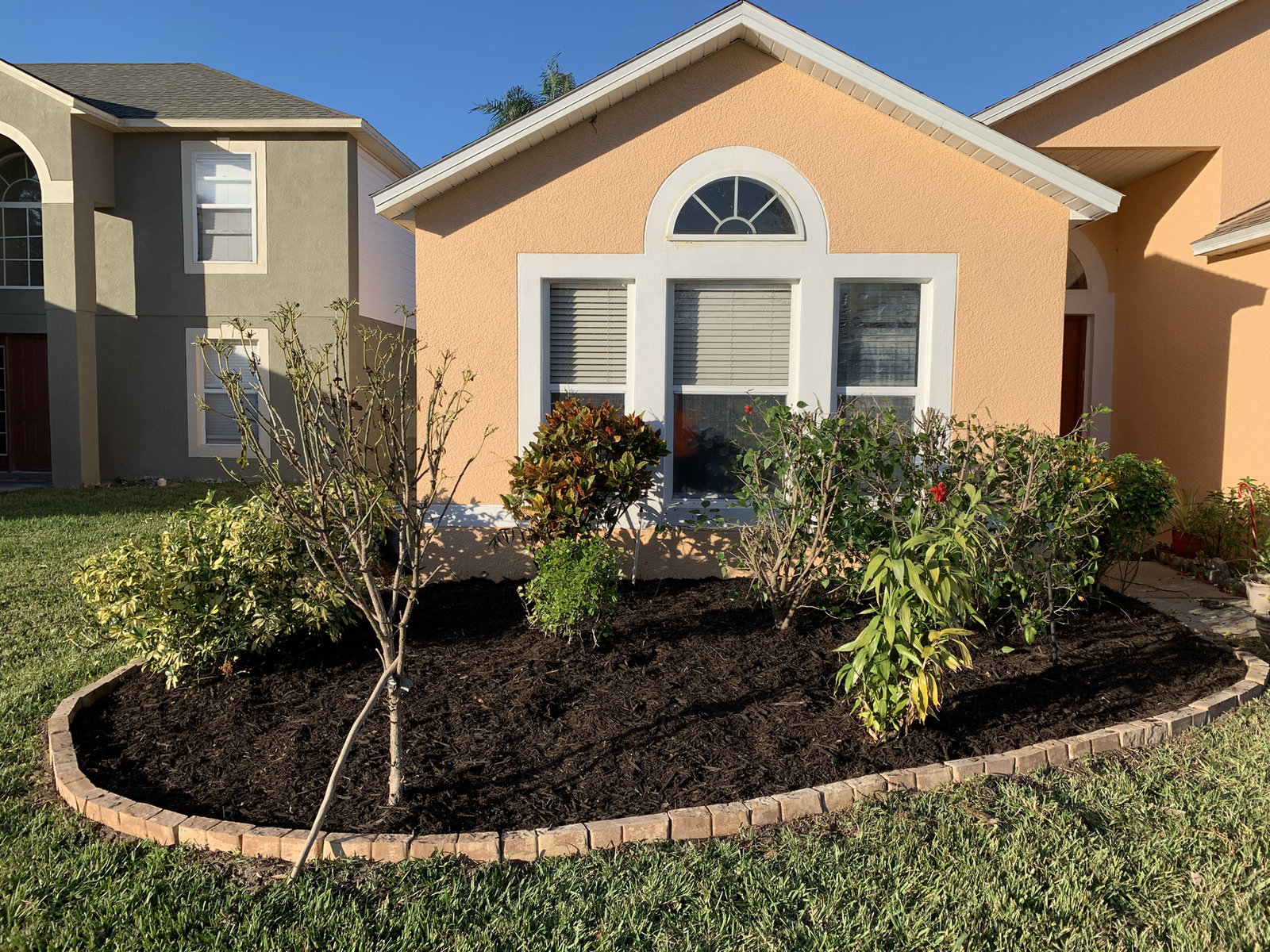New dark mulch bed with young plants and edging in front of a home