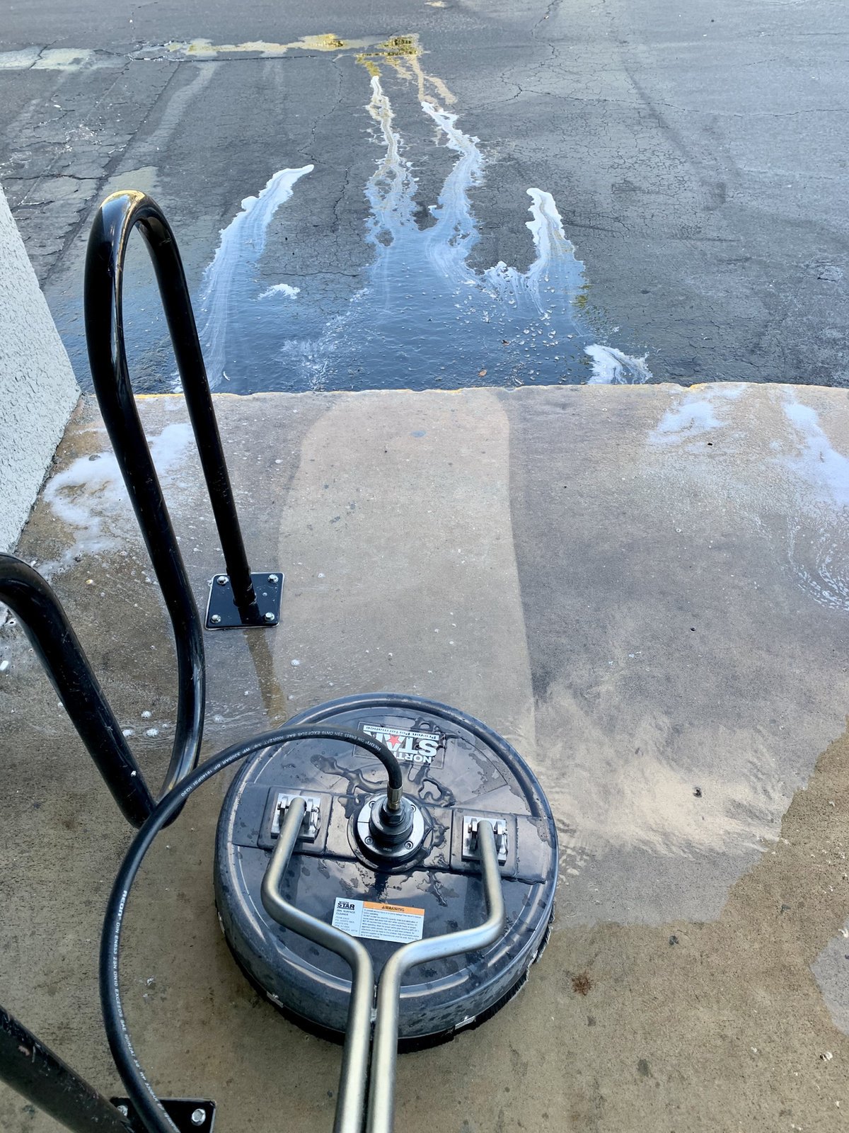 Surface cleaner pressure washing a concrete driveway, with clean and dirty sections side by side