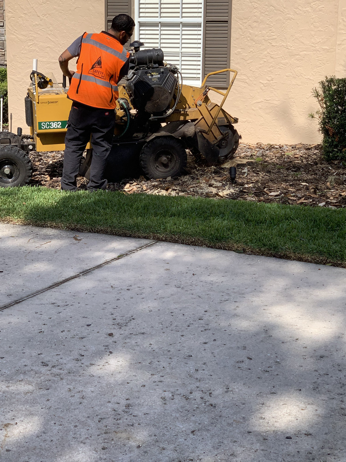 Worker in a hi-vis vest running a stump grinder at the edge of a lawn